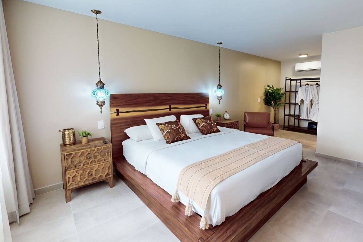 Une chambre spacieuse avec un grand lit, une tête de lit en bois et deux lampes suspendues.