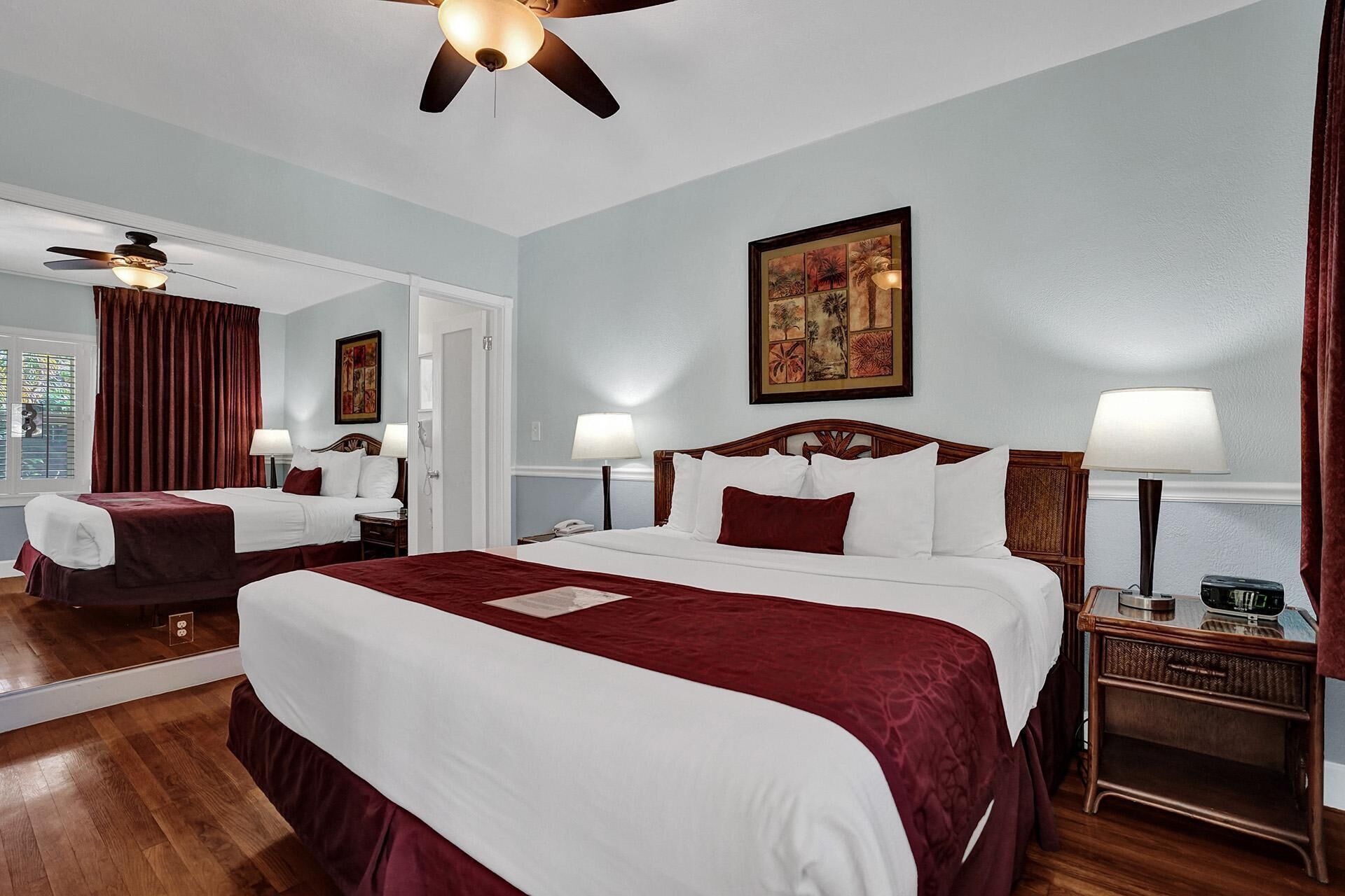 A hotel room with a large bed, two bedside tables, a ceiling fan, and a painting on the wall.