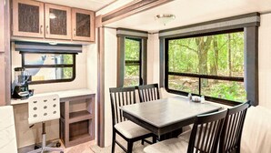 Una cocina compacta con comedor, ventanas amplias y vistas al bosque.