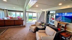 Un salon spacieux doté d’une grande télévision, de sièges confortables et offrant une vue sur l’extérieur.