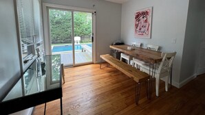Cocina moderna con un banco de madera, sillas blancas y vistas a una piscina a través del ventanal.