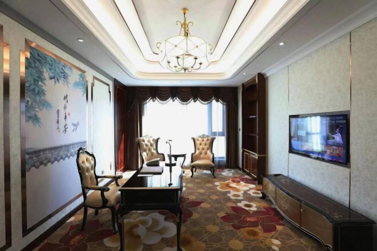A hotel room with a dining table, two chairs, a TV, and a large window.