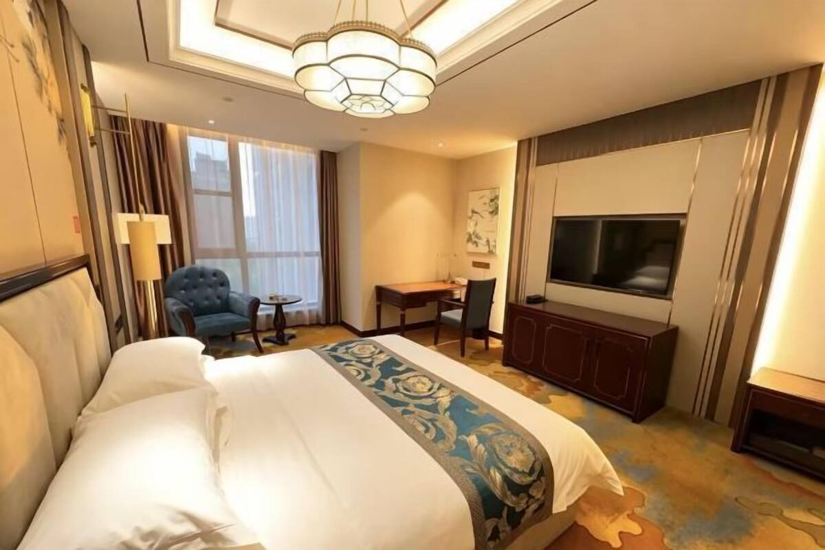 A hotel room with a large bed, a television, a desk, and a chair.