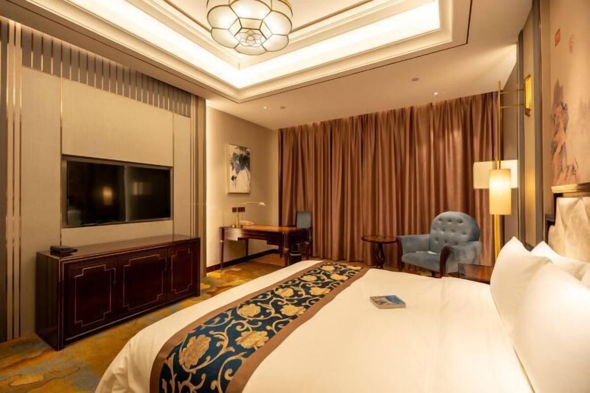 A hotel room with a large bed, a flat-screen TV, a desk, a chair, and a lamp.