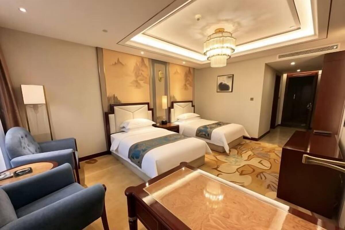 A hotel room with two beds, a desk, a chair, a chandelier, and a wall with a mountain design.