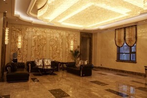 Eine großzügige Lobby mit hoher Decke, einer Sitzecke mit Sofas und einem Couchtisch sowie einem großen Fenster mit Vorhängen.