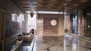 A spacious lobby with a marble floor, a large circular wall feature, and a ceiling with a geometric pattern.