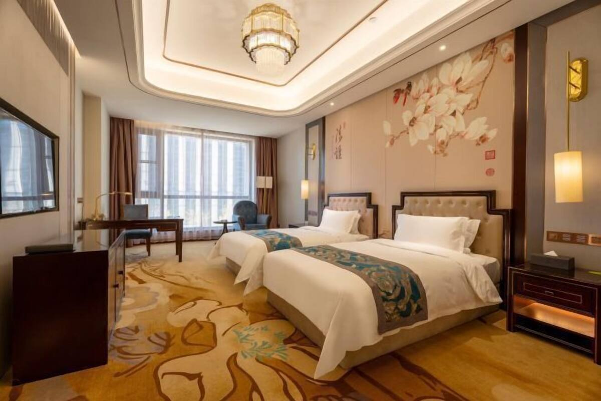 A hotel room with a large bed, a desk, a chair, and a large window.