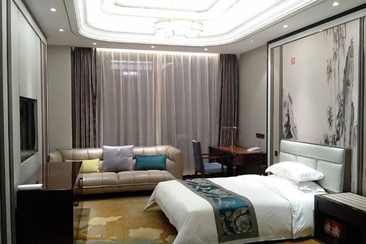 A hotel room with a bed, a sofa, a desk, and a large painting on the wall.