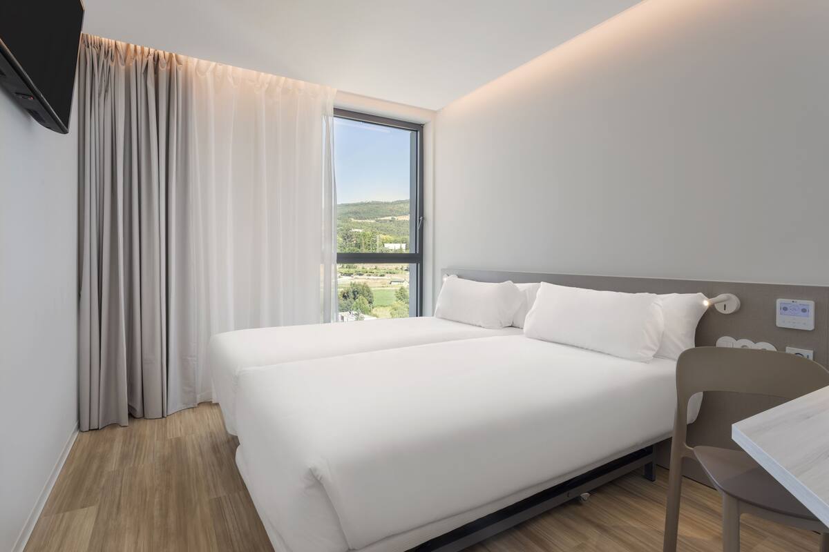 A modern hotel room with a large bed, a view of the countryside, and a desk with a chair.