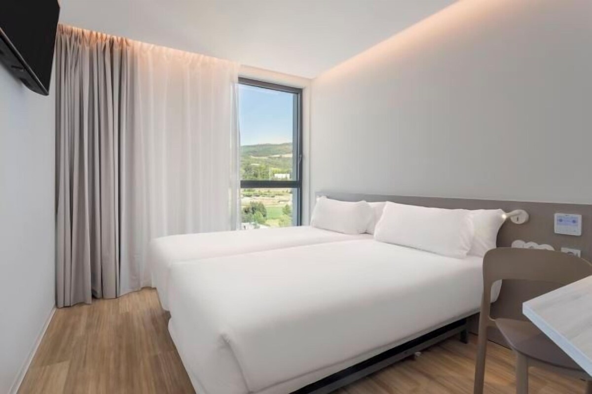 A modern hotel room with a large bed, a view of the countryside, and a flat-screen TV mounted on the wall.