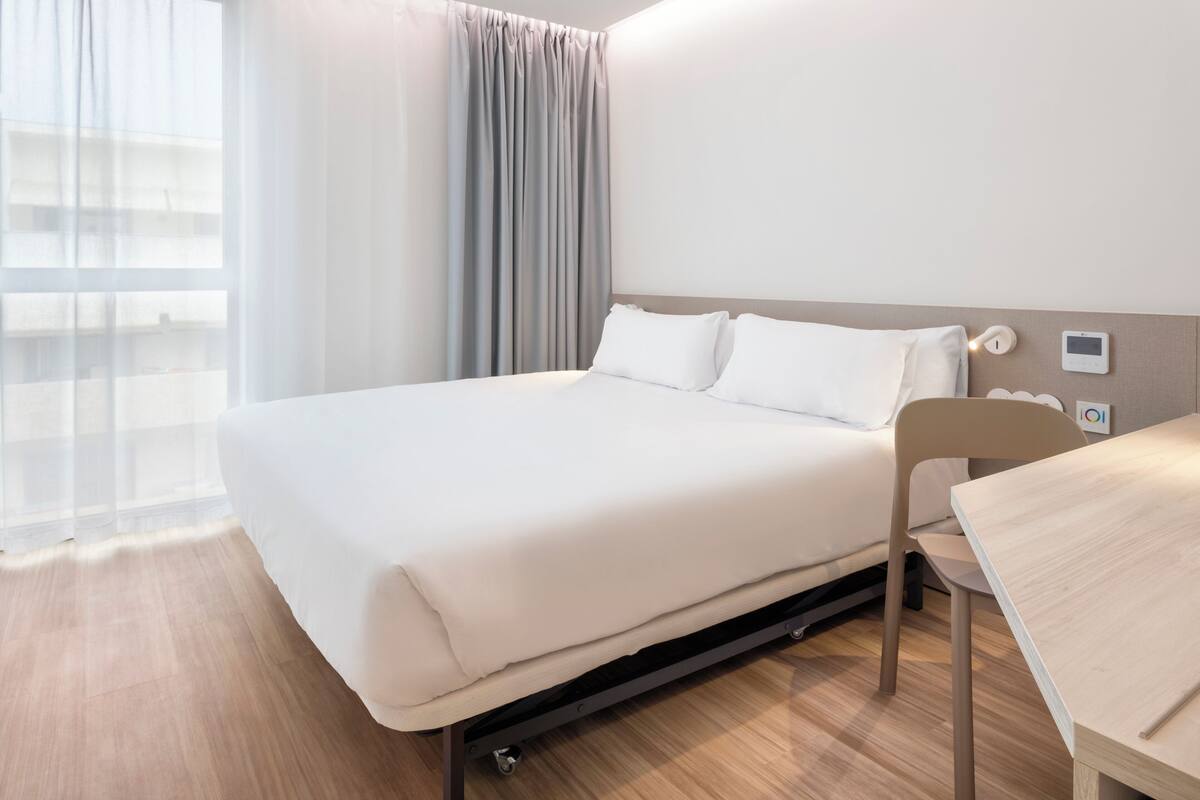 A modern hotel room with a large bed, a desk, and a chair.