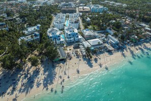 Vista aérea de una zona turística costera con varios edificios, una playa y palmeras.