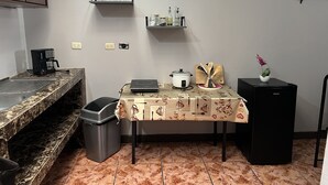 A compact kitchen with a marble countertop, a coffee maker, a sink, a trash bin, a table with a floral tablecloth, a slow cooker, a small refrigerator, and a potted plant. - Relax in downtown Alajuela / 5min near the Airport (Alajuela)