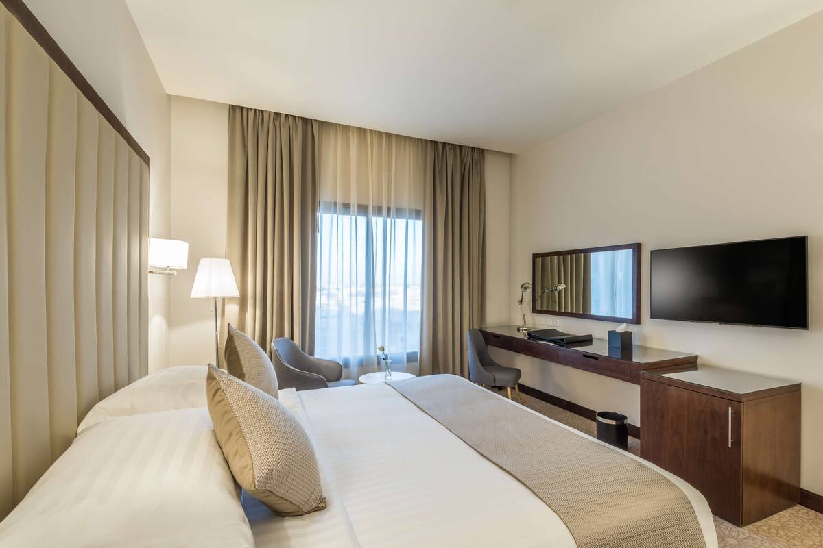 Ein Hotelzimmer mit Bett, Schreibtisch, Stuhl, Fernseher und Vorhängen.