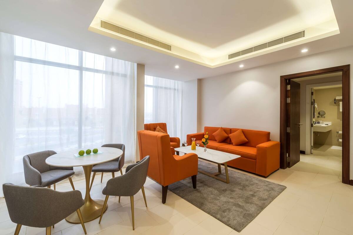 Ein modernes Wohnzimmer mit rundem Tisch, grauen Sesseln, einem orangefarbenen Sofa und einem Couchtisch.