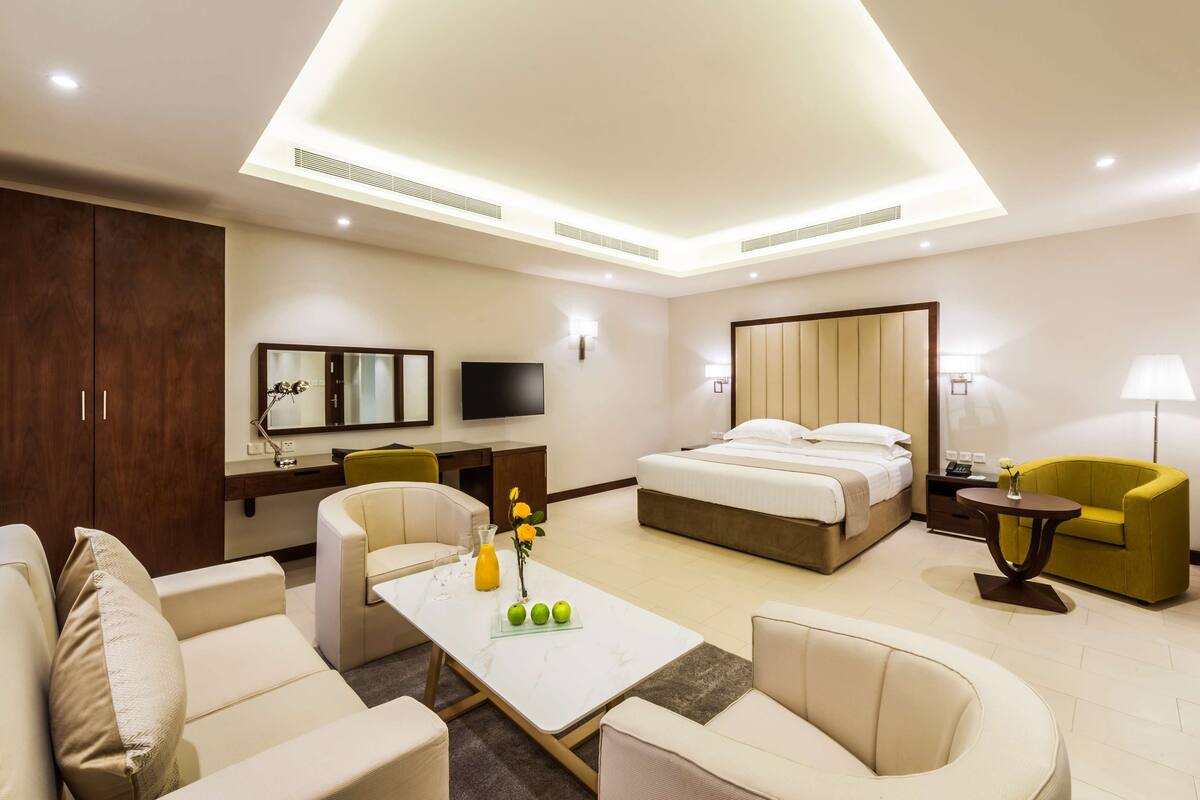 Ein modernes Hotelzimmer mit Bett, Sofa, Sessel und Schreibtisch mit Fernseher.