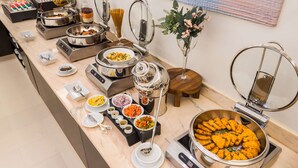 A buffet with various food stations, including a large bowl of orange-colored food, pasta, and other dishes.