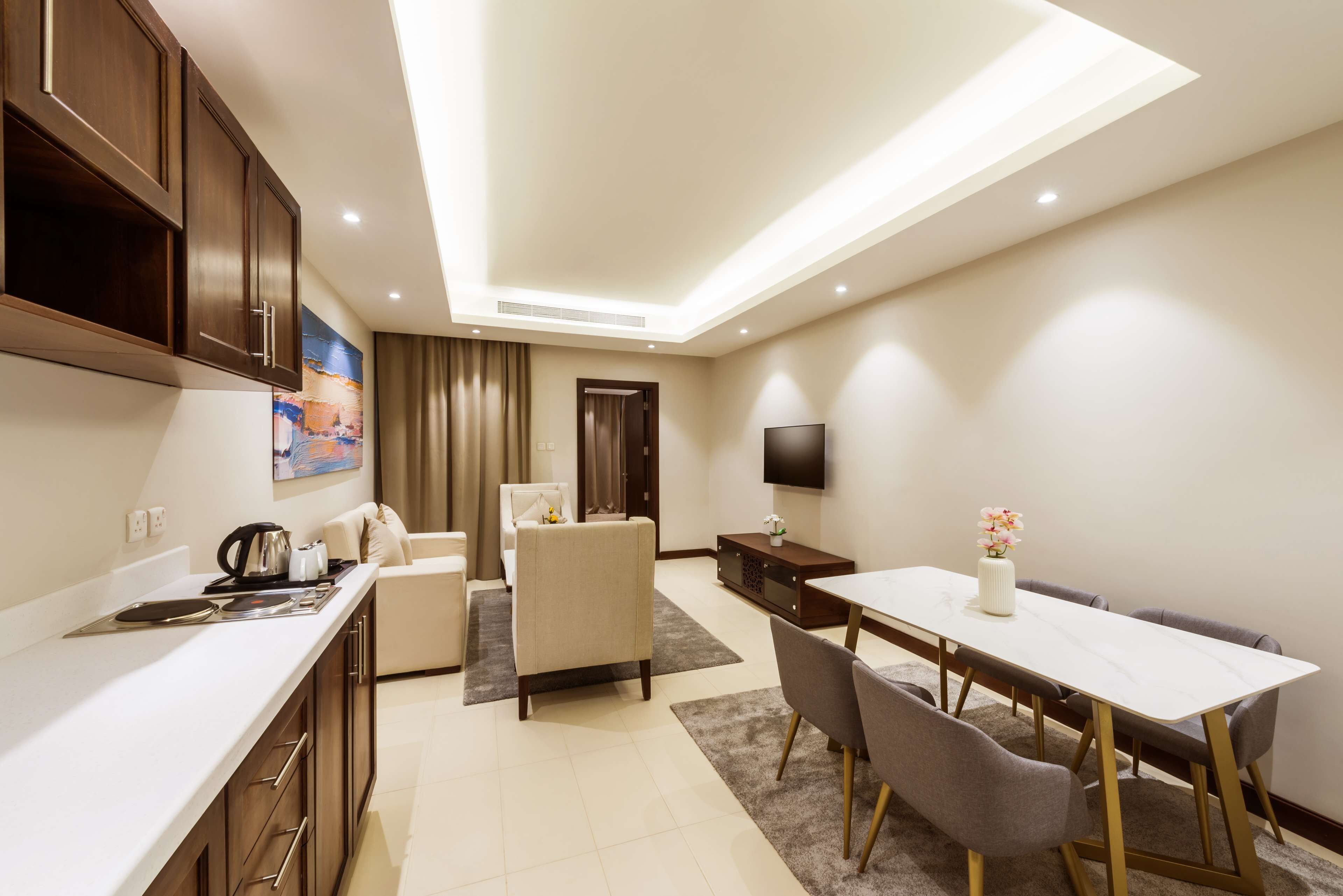 A modern hotel room with a kitchen, dining area, and a TV mounted on the wall.