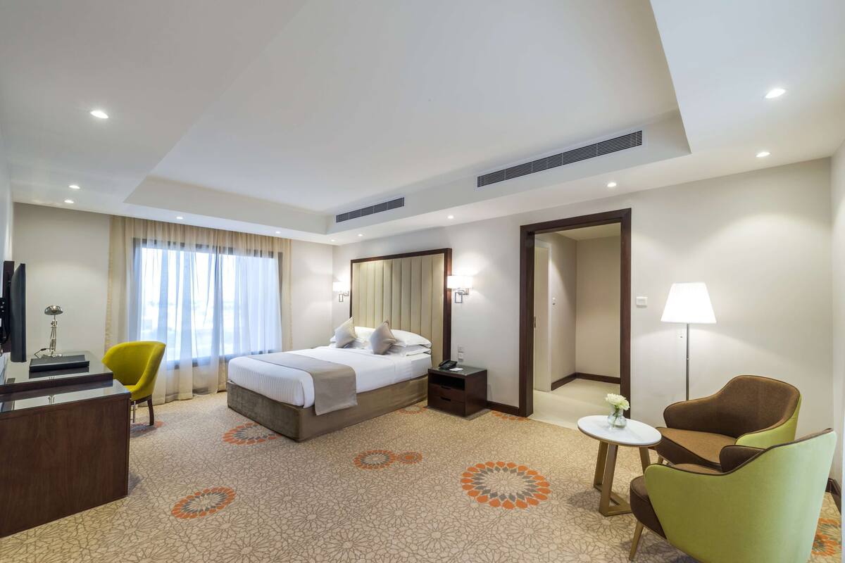 Ein Hotelzimmer mit Bett, Schreibtisch, Stuhl, Lampe und einem kleinen Tisch mit Blumen.