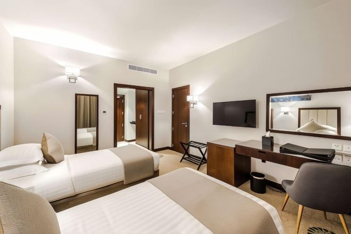 A hotel room with two beds, a desk, a chair, a TV, and a mirror.
