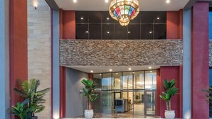 A modern building entrance with a large glass door, a decorative hanging light fixture, and potted plants.