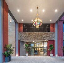 A modern building entrance with a large glass door, a decorative hanging light fixture, and potted plants.
