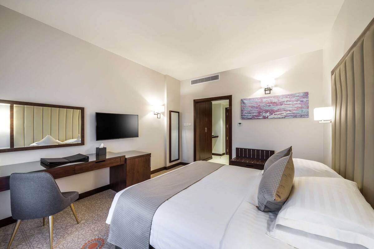Ein Hotelzimmer mit Bett, Schreibtisch, Stuhl, Fernseher und einem Gemälde an der Wand.