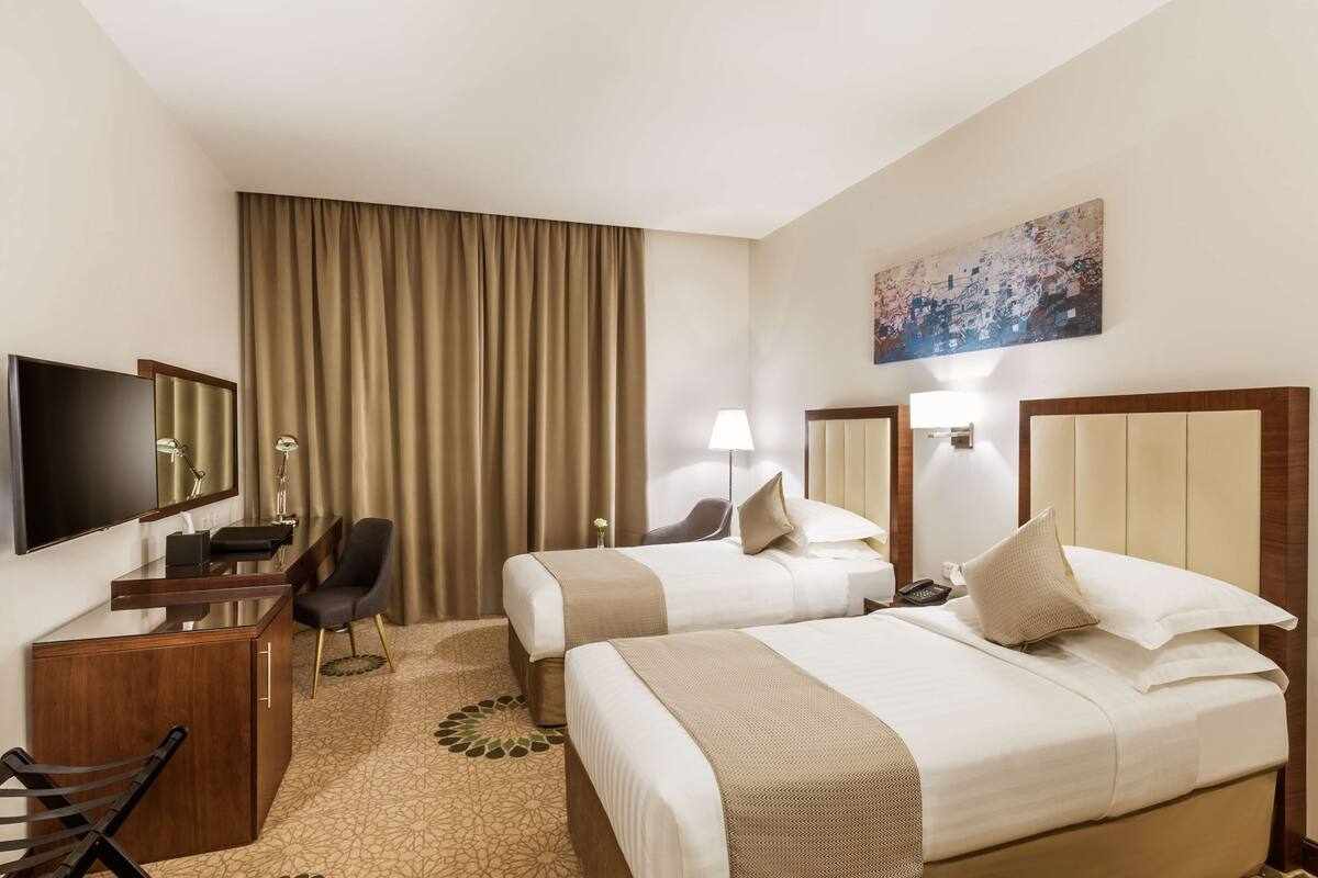 Ein Hotelzimmer mit zwei Betten, einem Schreibtisch, einem Sessel, einem Fernseher und einem Bild an der Wand.