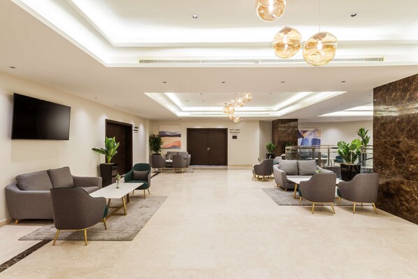 Eine moderne Lobby mit einem Flachbildfernseher, bequemen Sitzgelegenheiten und einem Marmor-Rezeptionstresen.
