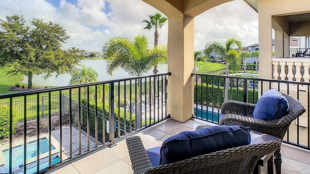 Un balcón con mobiliario de mimbre, piscina y vistas a un campo de golf y un lago.