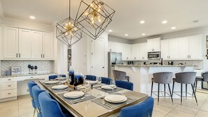Una cocina moderna con armarios blancos, una isla central con sillas azules e iluminación colgante.