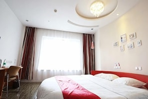 A hotel room with a large bed, a desk, a chair, a window with curtains, and a chandelier. - Aoliyang Business Hotel (Zhuanghe Jinma Plaza) (Zhuanghe)