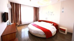 A hotel room with a round bed, a wooden desk, a television, and a large window with curtains. - Aoliyang Business Hotel (Zhuanghe Jinma Plaza) (Zhuanghe)
