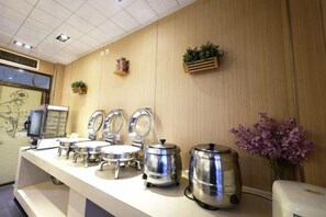 A buffet setup with multiple serving stations, a coffee machine, and decorative plants. - Aoliyang Business Hotel (Zhuanghe Jinma Plaza) (Zhuanghe)