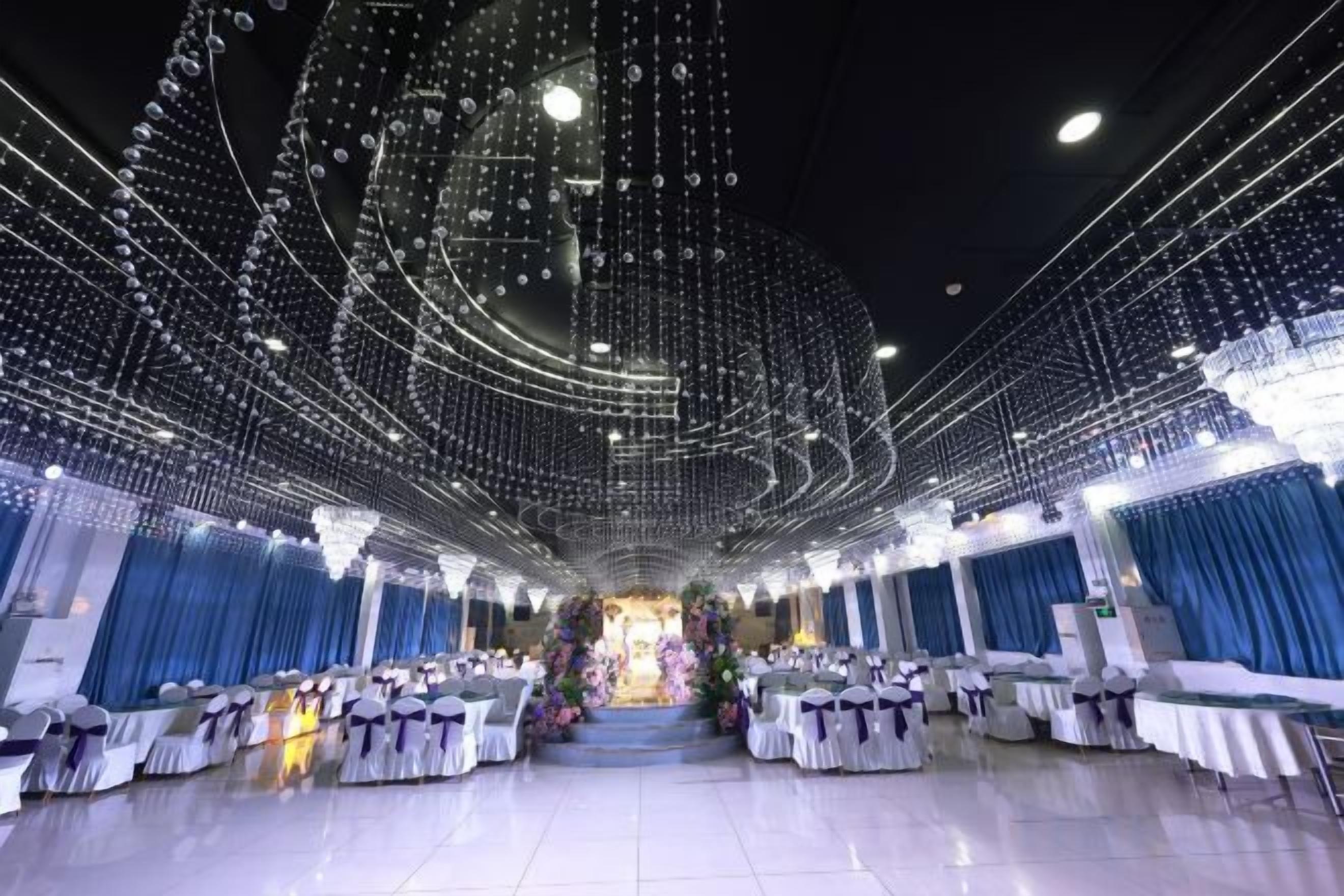 A banquet hall with rows of tables, a chandelier, and draped curtains.