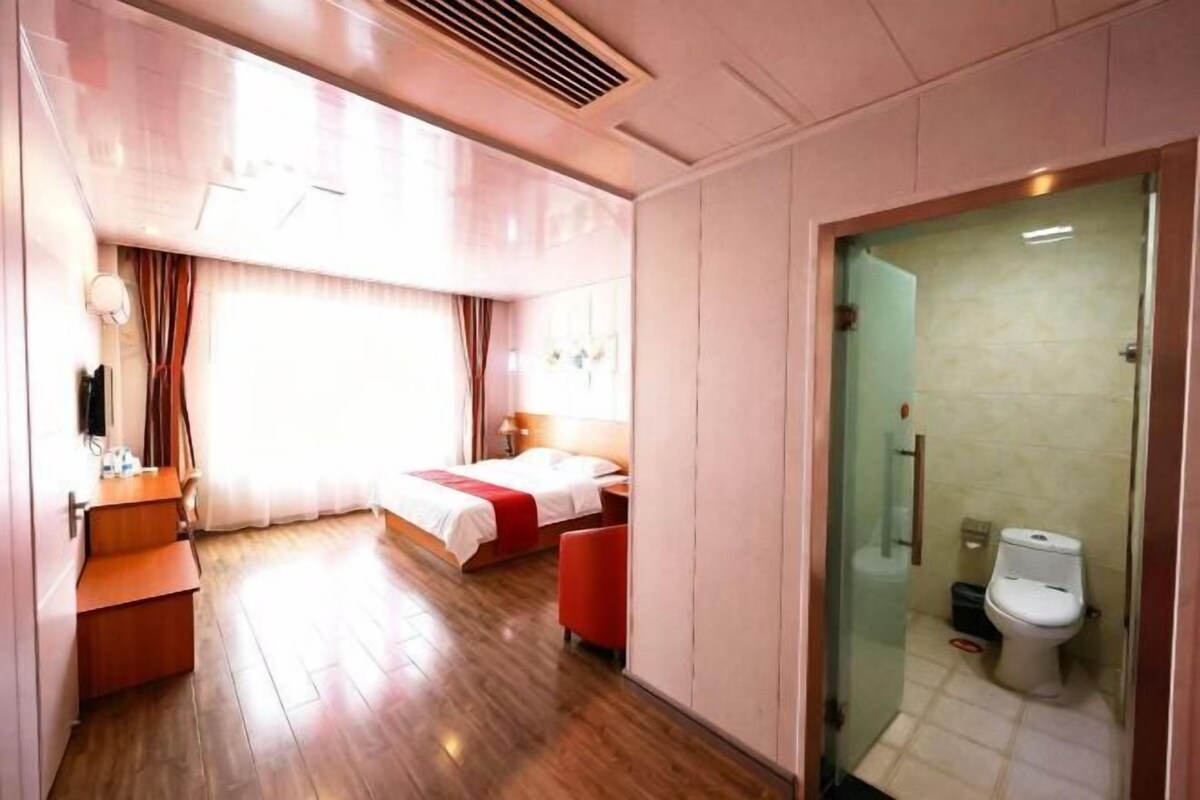 A hotel room with a bed, a desk, a chair, a bathroom with a toilet, and a shower area.