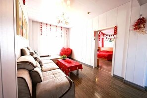 A room with a sofa, a small table with a red tablecloth, and a bed with red bedding. - Aoliyang Business Hotel (Zhuanghe Jinma Plaza) (Zhuanghe)