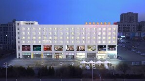 A multi-story hotel with a row of rooms on the ground floor, a central atrium with large windows, and a parking lot in front. - Aoliyang Business Hotel (Zhuanghe Jinma Plaza) (Zhuanghe)