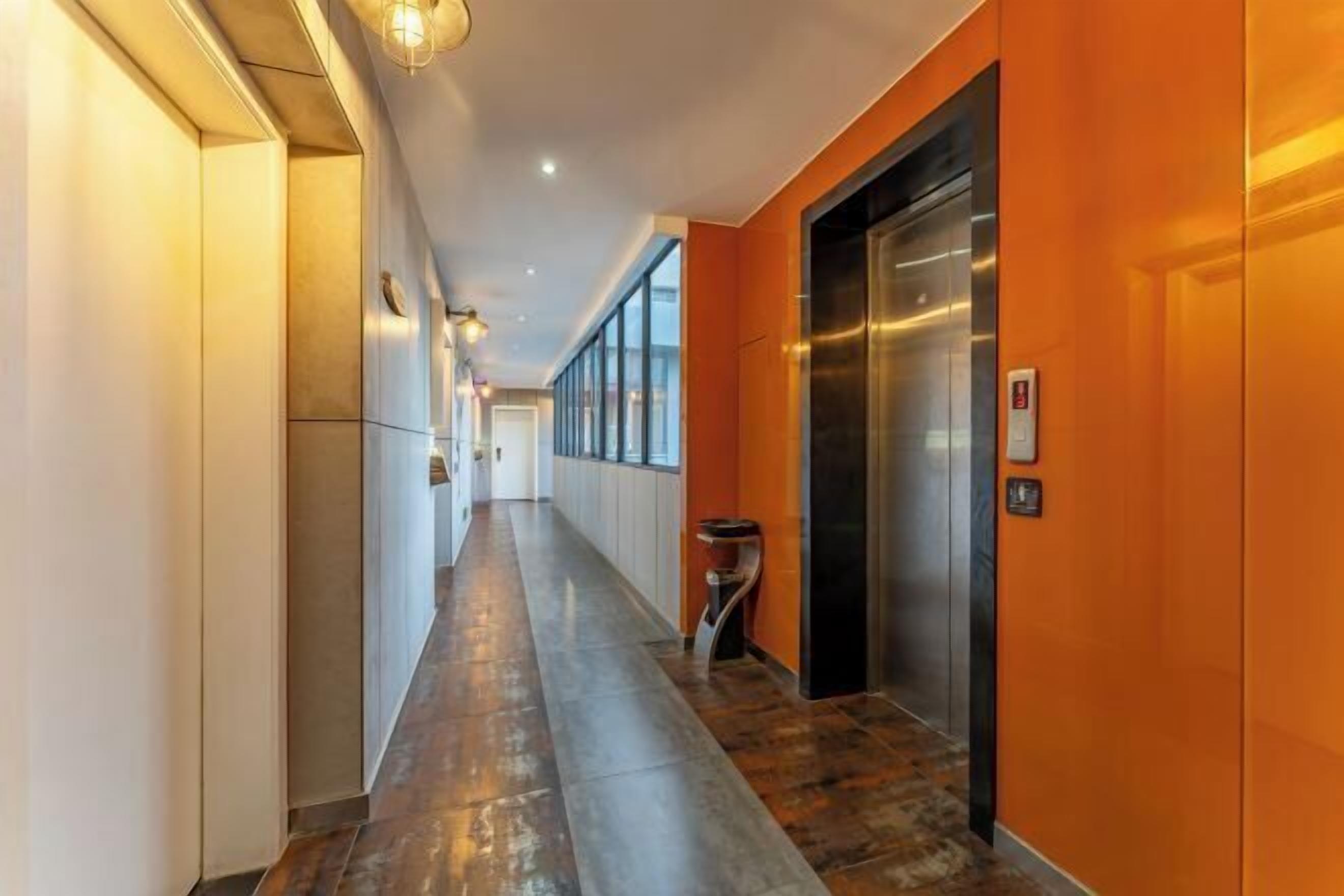 A long, narrow hallway with a polished floor, an elevator, and a wall-mounted light fixture.