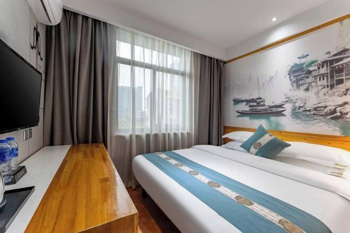 Habitación de hotel con cama, un banco de madera, un televisor y un mural con una escena de río.