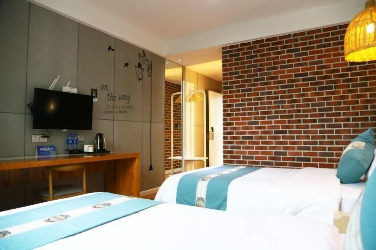 Habitación de hotel con televisión, escritorio, cama con cubrecama azul y blanco, y pared de ladrillo.