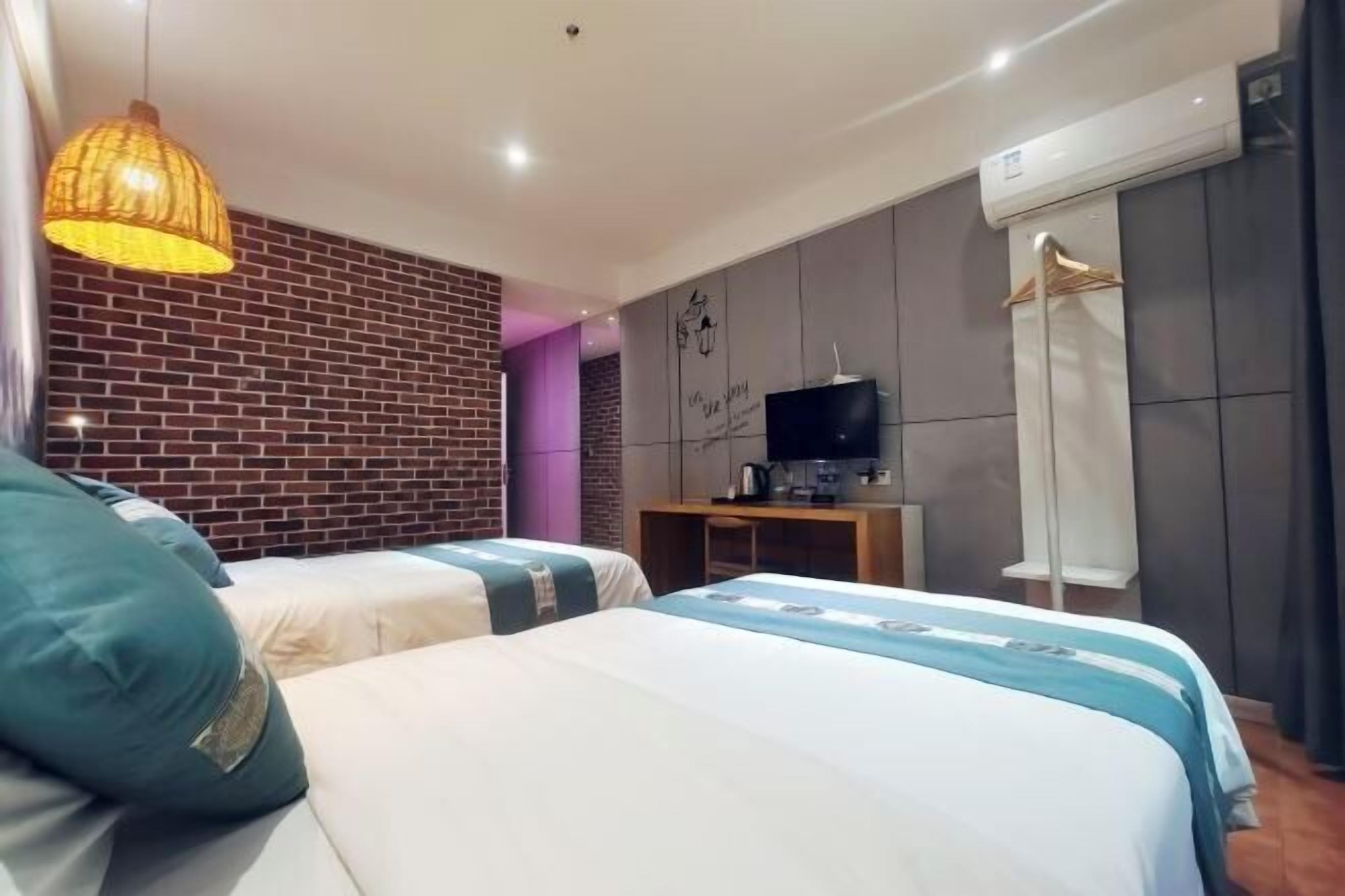 A hotel room with two beds, a television, a wardrobe, and a brick wall.