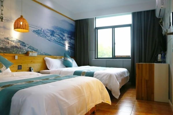 Una habitación de hotel con dos camas, un ventanal con cortinas, cabecero de madera y un mural en la pared.