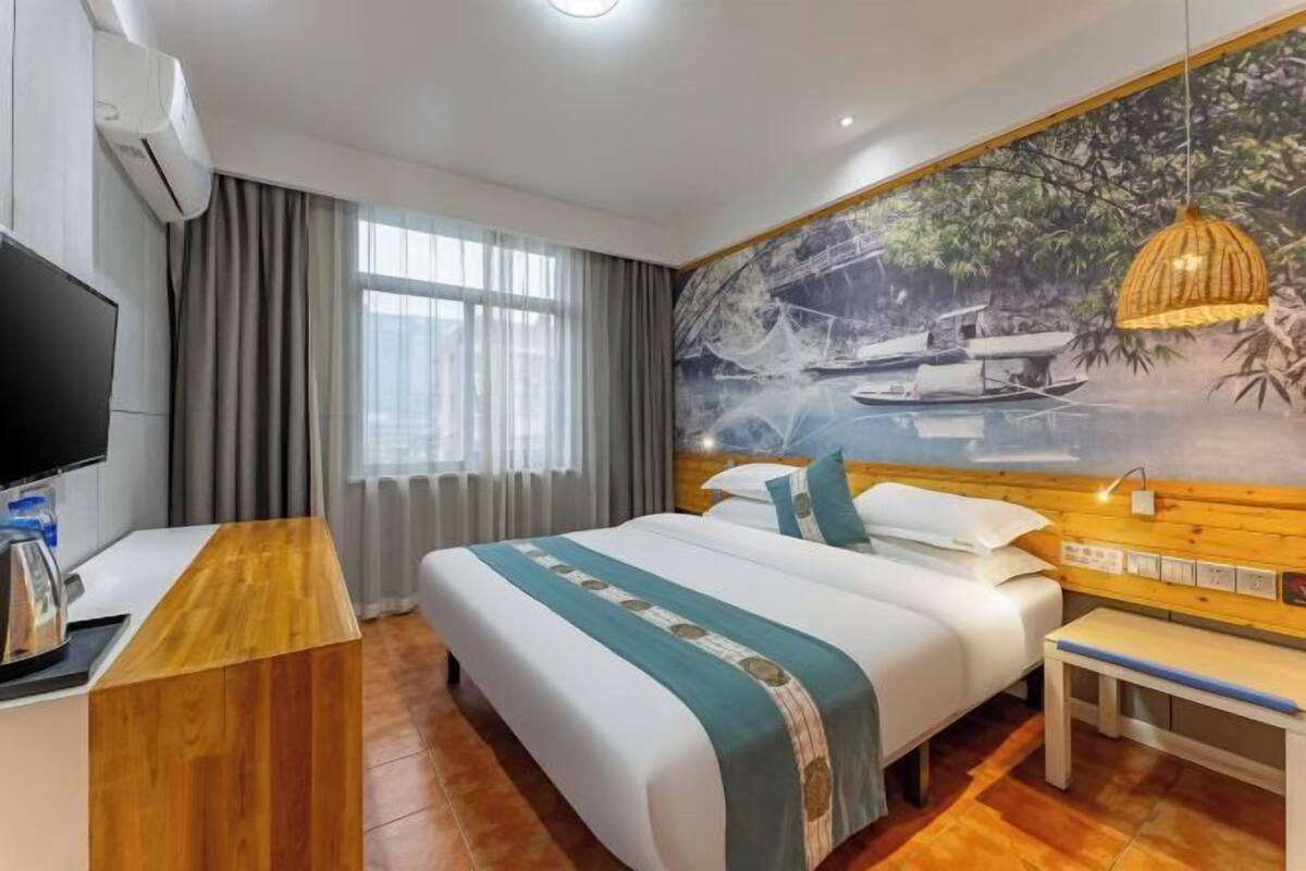 Una habitación de hotel con cama, escritorio, televisor y un mural de un barco en el agua.