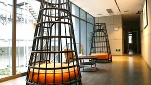 A modern interior with tiered black metal chairs with orange cushions, a glass wall, and a staircase in the background. - Jinbo Hotel (Yichang)