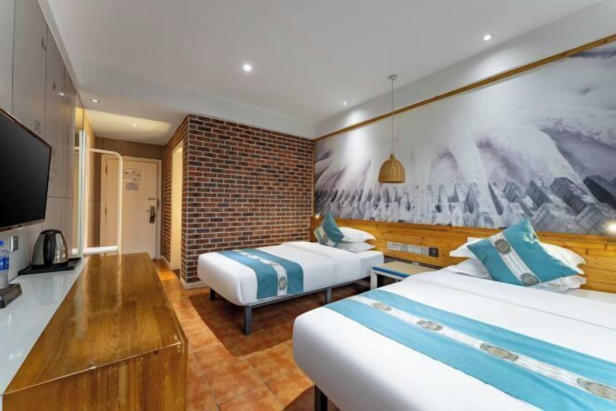 Habitación de hotel con dos camas, televisión, cafetera y pared de ladrillo.