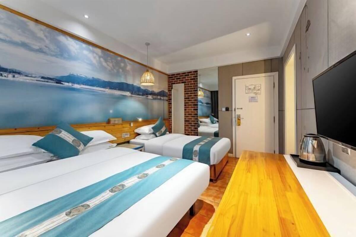 Habitación de hotel con dos camas, una mesa de madera, un televisor y un mural de un paisaje.