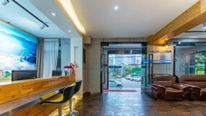 A hotel reception area with a wooden reception desk, two bar stools, a seating area with leather sofas, and a large window offering a view of the street. - Jinbo Hotel (Yichang)