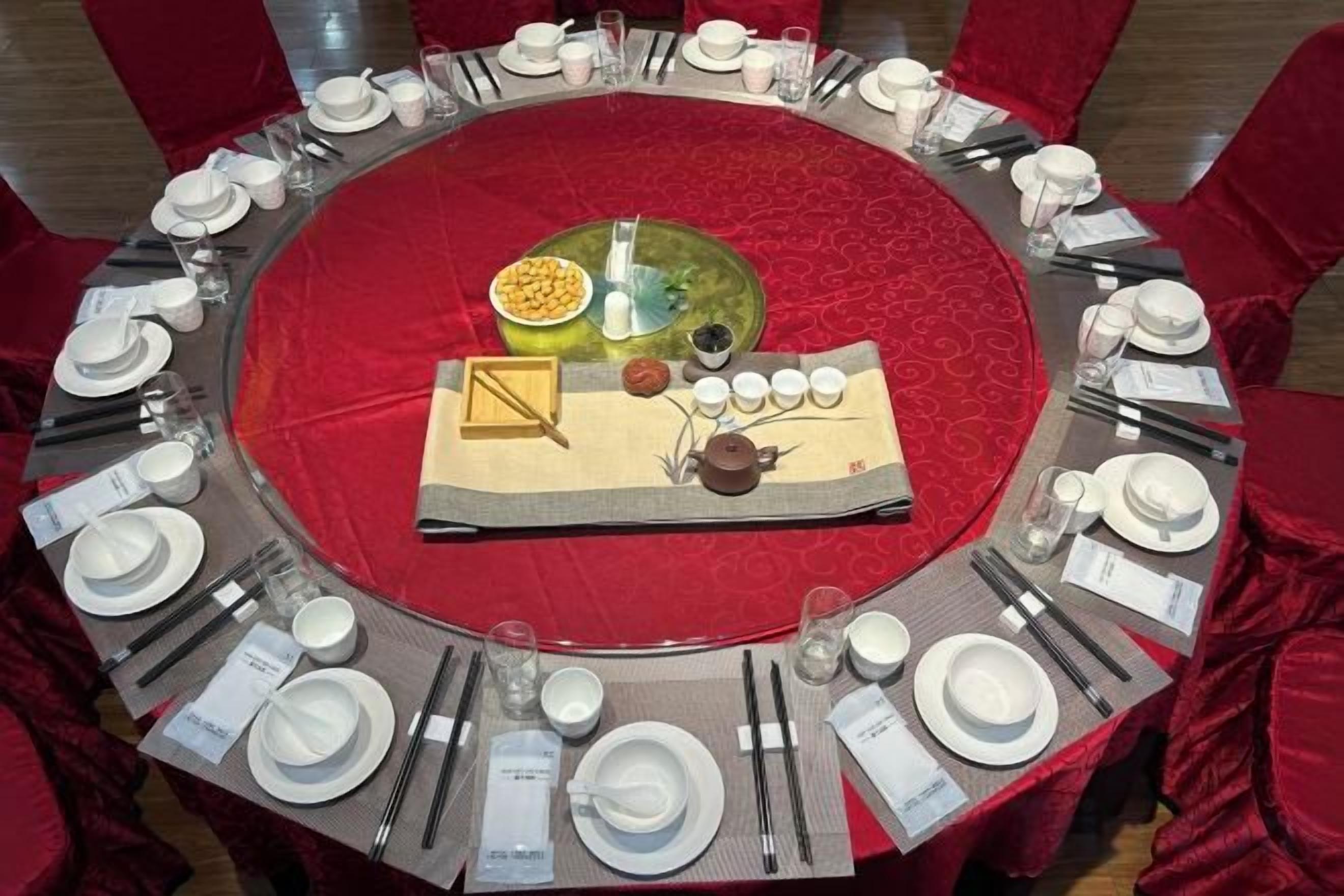 A round table set for a meal with a red tablecloth, surrounded by red chairs.